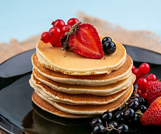 front-view-of-pancakes-with-red-and-black-currants-and-strawberries-on-black-plate-on-beig