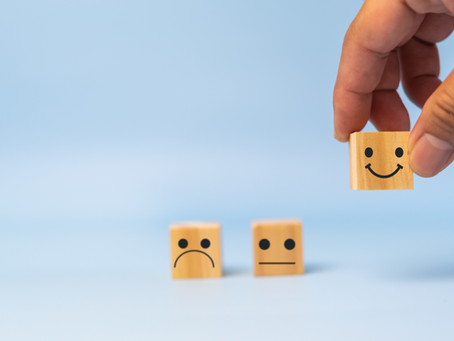 A hand places a wooden block with a smiling face beside blocks with neutral and sad faces, symbolizing positive feedback and encouragement.