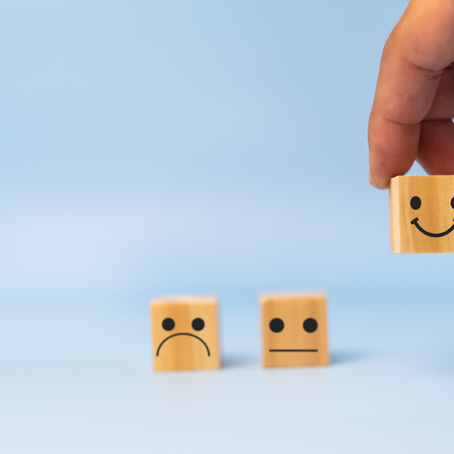 A hand places a wooden block with a smiling face beside blocks with neutral and sad faces, symbolizing positive feedback and encouragement.