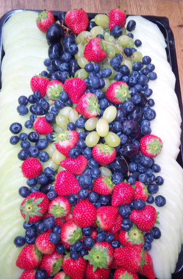 Large platter filled with sliced melon, decorated with grapes, strawberries and blueberries
