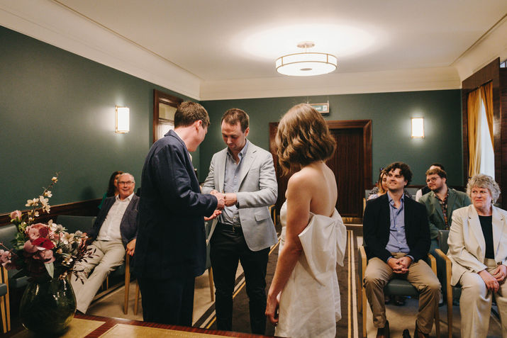 Best man handing the wedding rings to the groom during the ceremony. Hackney Town Hall.