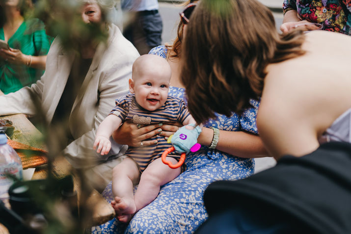 Baby laughing at the bride while sitting on a woman’s lap. Hackney, London.
