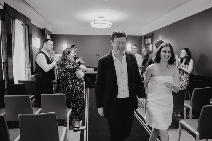 Just married couple walking hand in hand past cheering witnesses after the ceremony at Hackney Town Hall, London.
