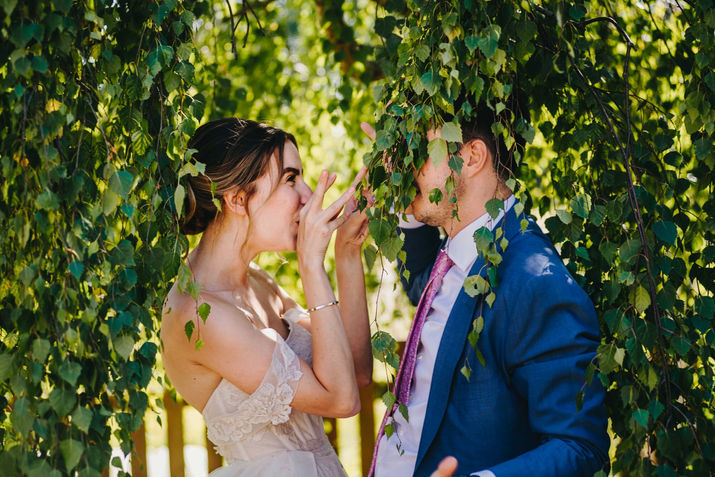 Bride makes funny faces at her groom under tree leaves. Wedding in a family farm in Hildenborough, Kent.