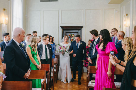 Bride and father walking down the aisle at the register office, greeted by witnesses at Chelsea Old Town Hall, London.