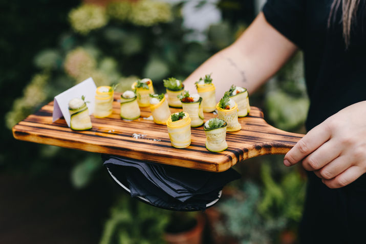 Close-up of a courgette canapé on a serving tray with a burnt stripe pattern, held by a waiter offering it to guests at The Hackney, London.