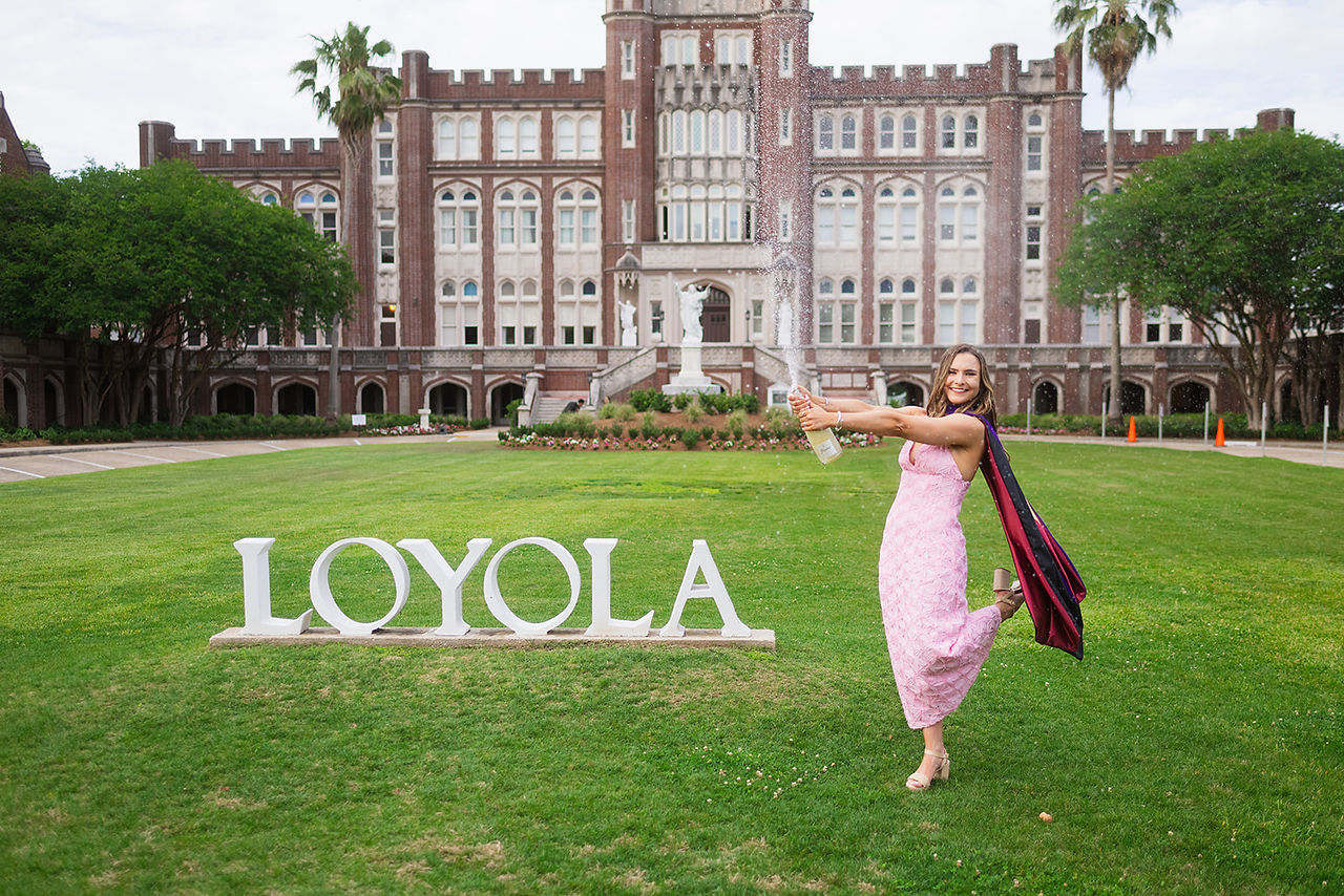 Loyola Law Graduate spraying champagne in front of the Loyola sign