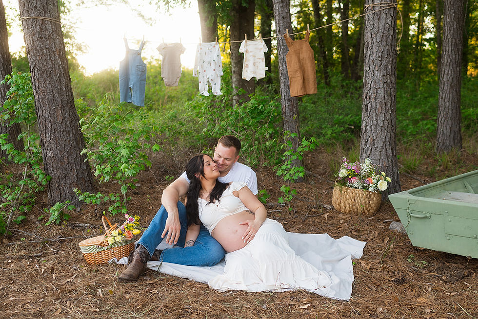 a couple lying on a picnic blanket with baby clothes behind them during their maternity session