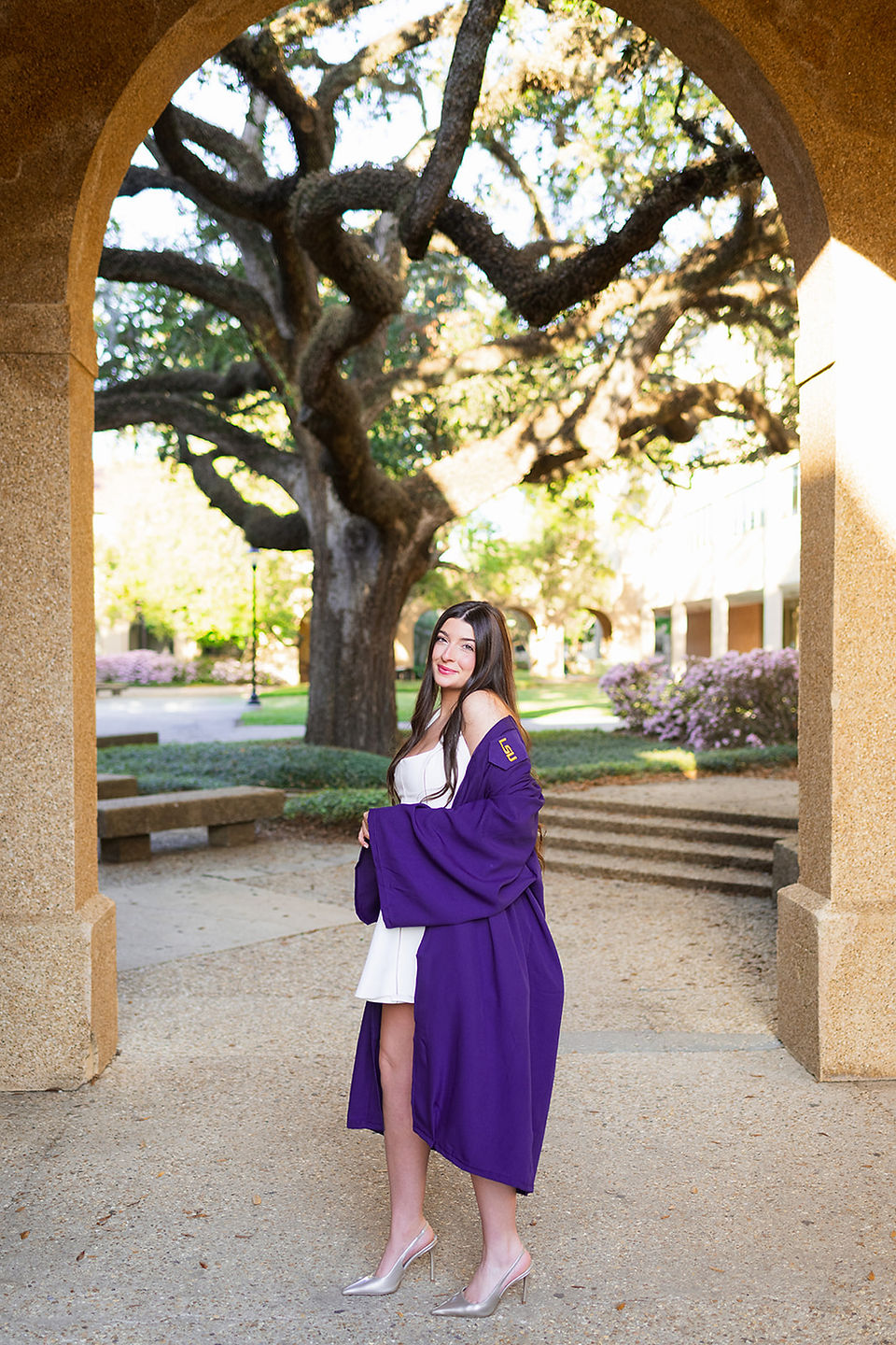 LSU senior in her graduation gown under an archway with oak trees in the background