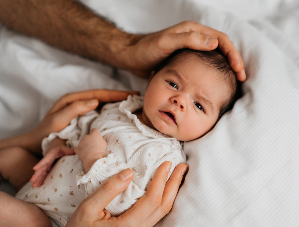 Neugeborenes Baby zu Hause eingekuschelt auf dem Bett bei einem entspannten Newborn Shooting