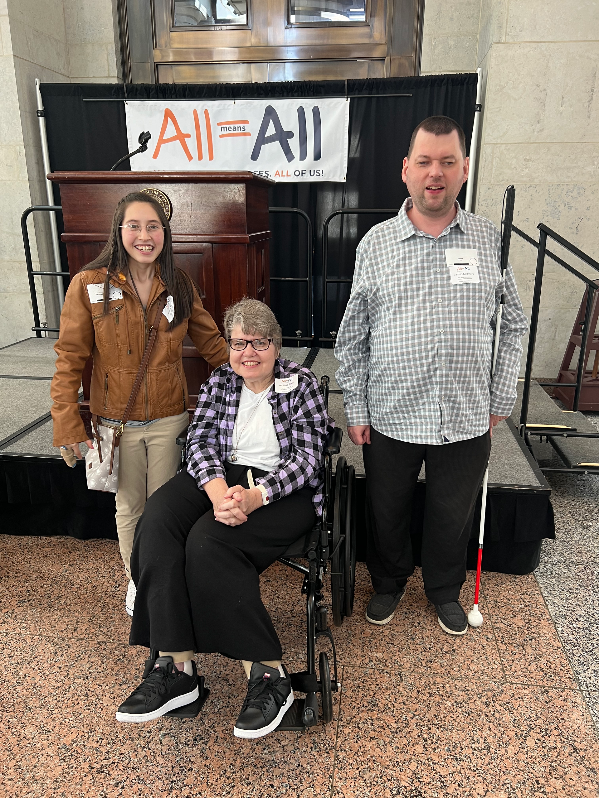 A teenage girl on the left, a woman in a wheelchair in the middle and a man on the right