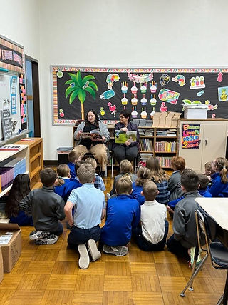 Two women reading a book to a group of children in a classroom. 