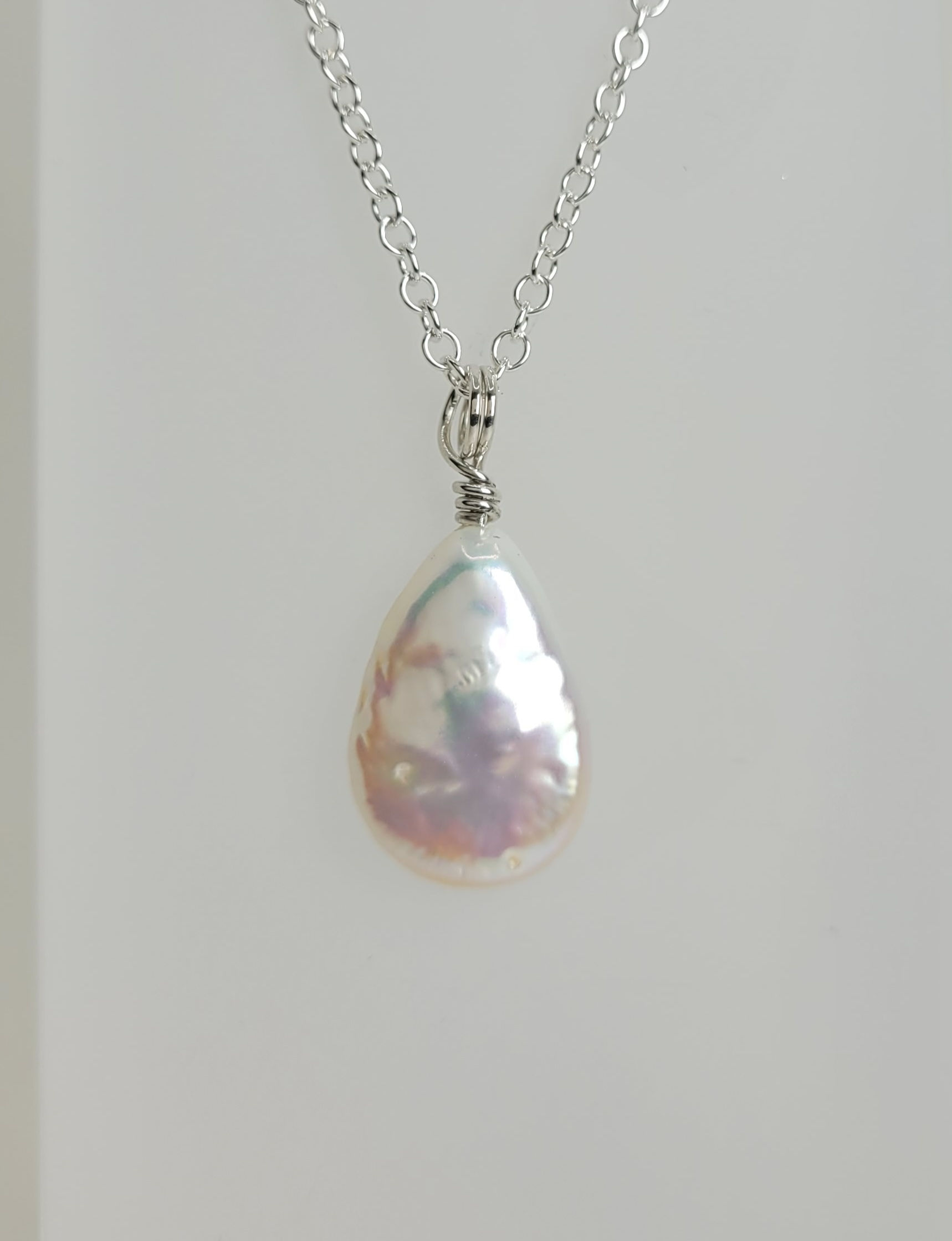 A simple teardrop shaped creamy textured pearl is avouch one inch long and hangs from a silver chain