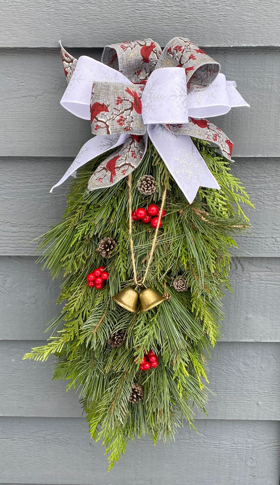 Decorative evergreen swag adorned with a white bow, red berries, and golden bells.