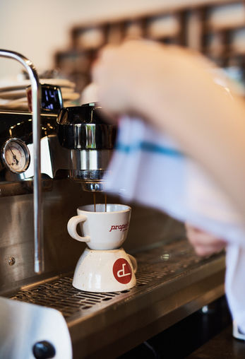 Candid close-up portrait of a barista performing an espresso pull, using a custom mirror reflective surface to monitor the technical quality of the shot.