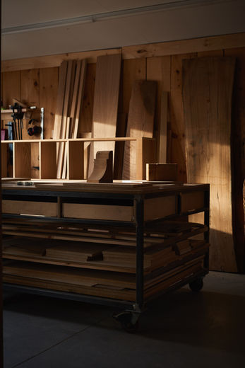 Minimalist commercial shot of a large live-edge wood slab resting on an industrial rolling rack in a professional woodshop.