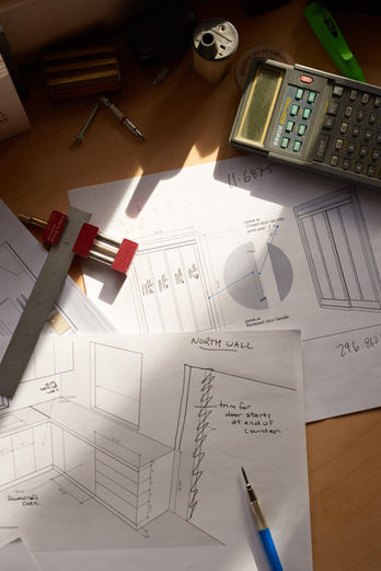 High-fidelity flat lay of technical woodworking blueprints, a pencil, and a calculator on a sun-drenched workshop desk.