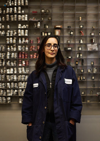 Professional portrait of a female lab technician in a blue coat standing before a sample library at MMM Metal.