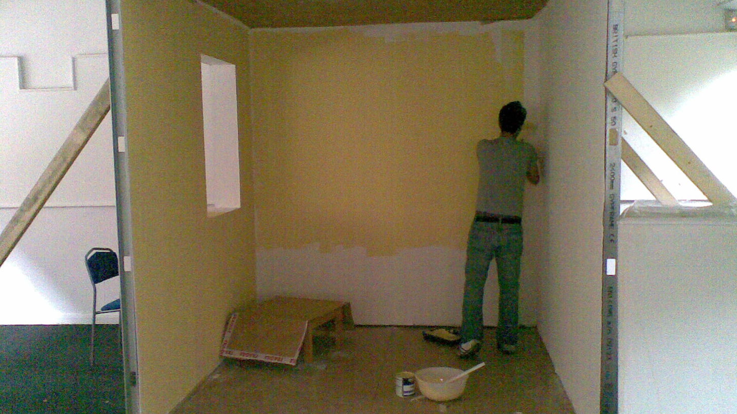 Artist painting the interior walls of the constructed room during installation process.