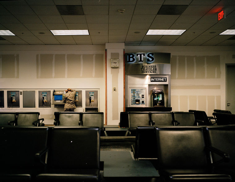 Empty waiting area with rows of chairs and public telephones in a transit or service hall.
