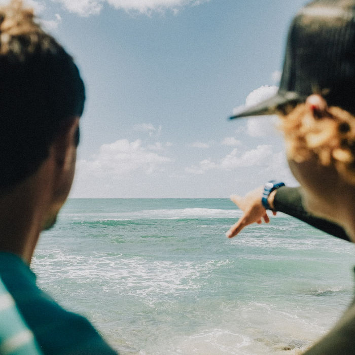 Two people looking out at the ocean, one pointing toward the waves