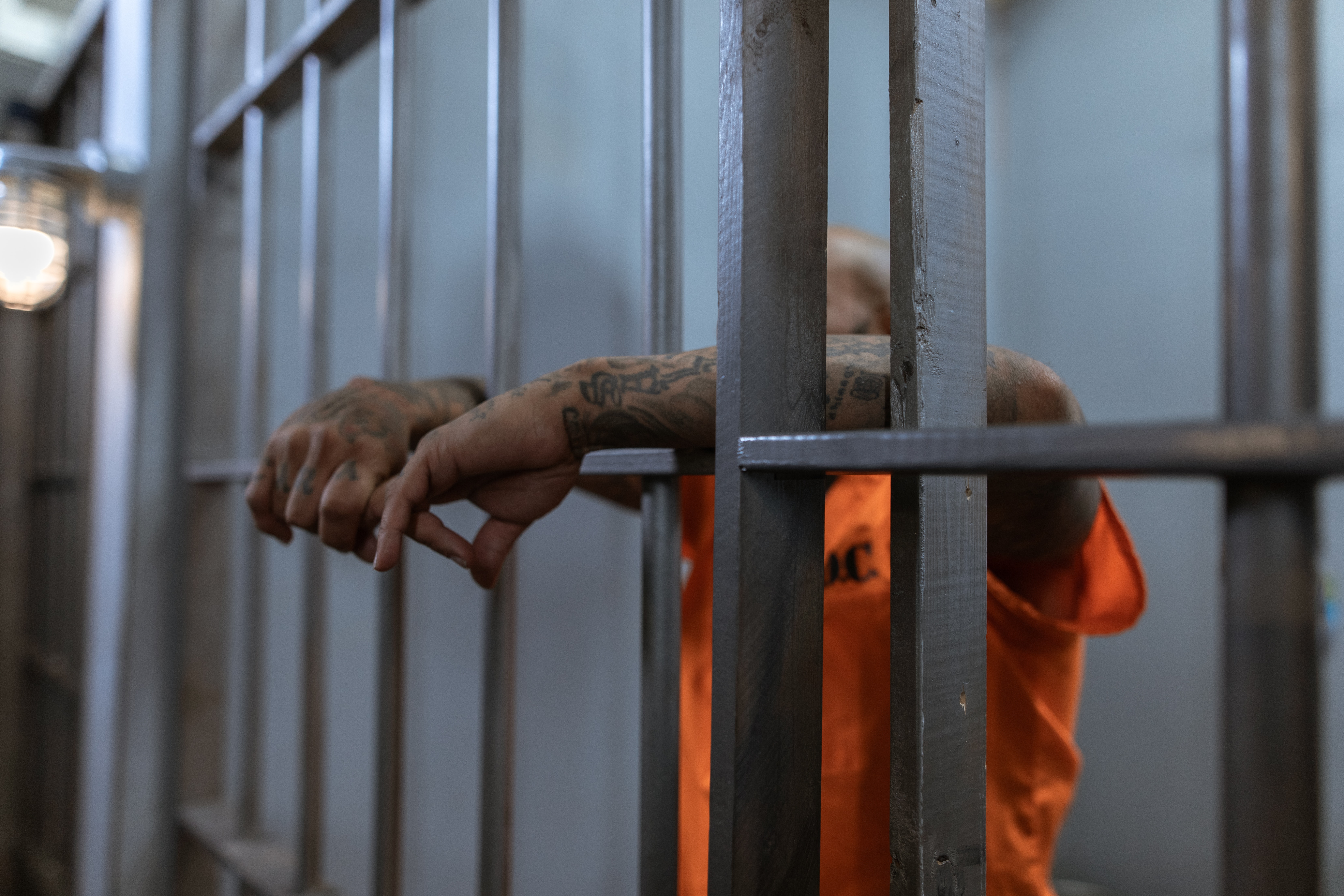 A man in Orange Shirt with Tattooed Arms behind bars