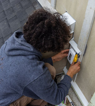 Residential electrician performing a weather-proof outlet installation on a home exterior.