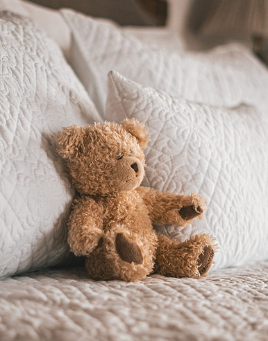 A brown teddy bear sits on a soft white fluffy pillow