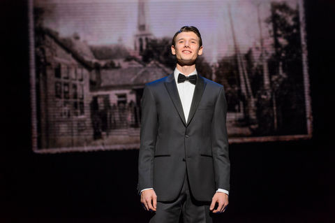 a man in a tuxedo and bow tie stands on a stage