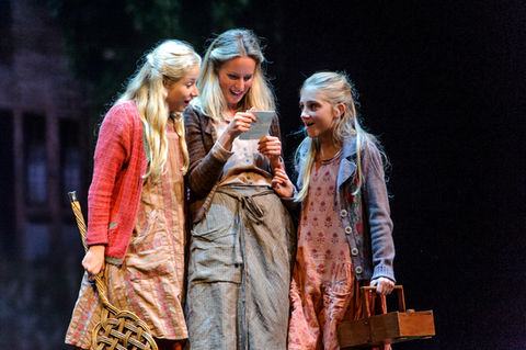 three girls are looking at a tablet together on a stage