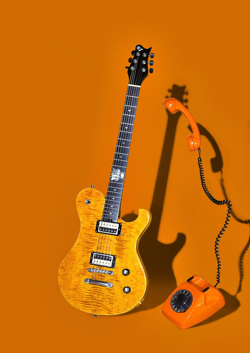 Künstlerisches Stillleben mit E-Gitarre und orangem Wählscheibentelefon vor monochromem Hintergrund. NRW. Köln. Bonn