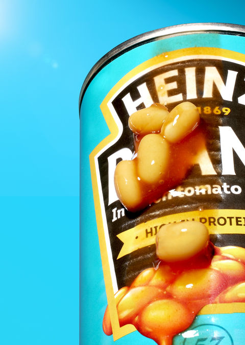 Nahaufnahme einer Heinz Baked Beans-Dose mit überlaufender Tomatensoße und Bohnen vor blauem Hintergrund. Kreative Foodfotografie von David Weimann aus Köln für moderne Markenauftritte in NRW.