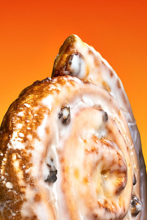 Makroaufnahme einer glasierten Zimtschnecke vor leuchtend orangem Hintergrund