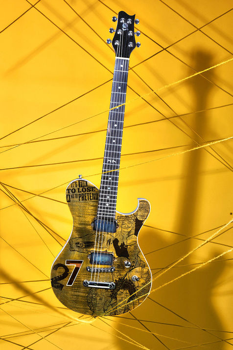 Custom E-Gitarre mit gealtertem Gold-Finish und Relic-Look vor gelbem Studiohintergrund mit gespannten Fäden und markanten Schatten.