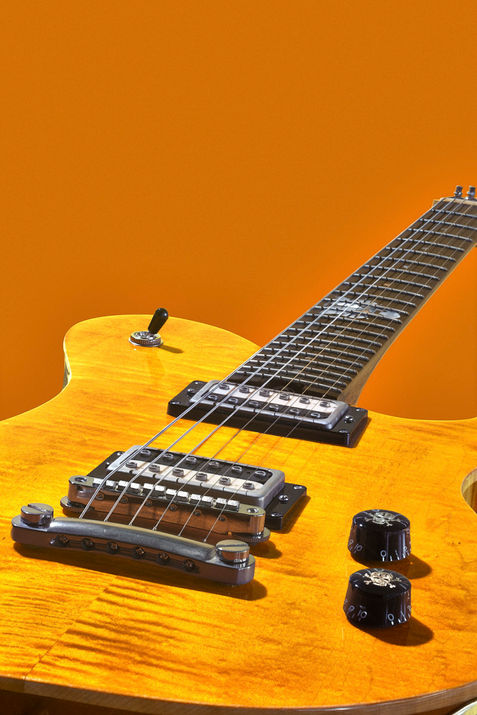 Detailaufnahme einer elektrischen Gitarre mit Humbuckern, schwarzer Hardware und markanter Maserung der Ahorndecke vor orangem Hintergrund. Qcumber Guitars Köln