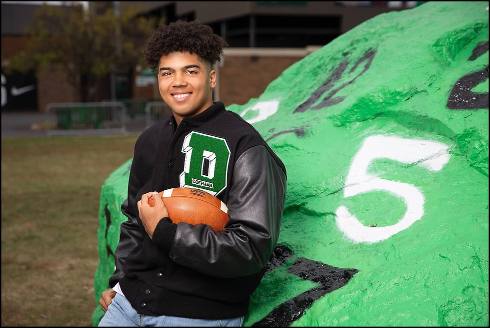 dublin coffman high school senior guy wearing letterman jacket holding football beside school rock