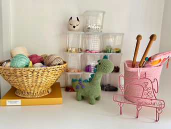 a basket of threads, clear plastic containers with buttons inside them, a grin crochet dinosaur sits infant of the buttons, a pink soft basket holds wooden knitting needles and a wire sign of a pink sewing machine and words saying I love sewing