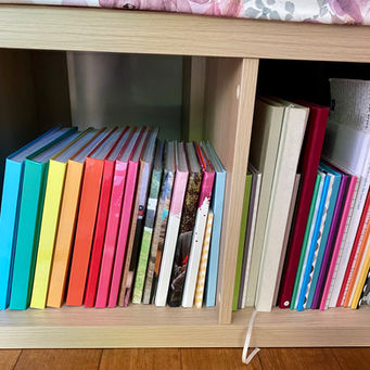 a rainbow of books in a cube bookshelf the sits under a bench seat