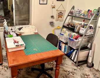 table with cutting mat with a rolling chain, a free-standing glass shelf unit is nearby housing all the things need for scrapbooking in a neat and orderly way