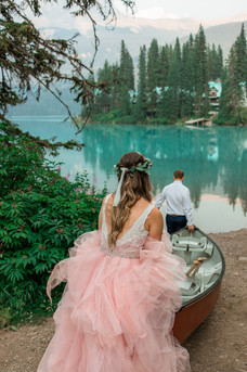 Woman in blush wedding dress helps groom with canoe