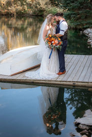 Bride and groom standing closely together on pond pier next to overturned small boat