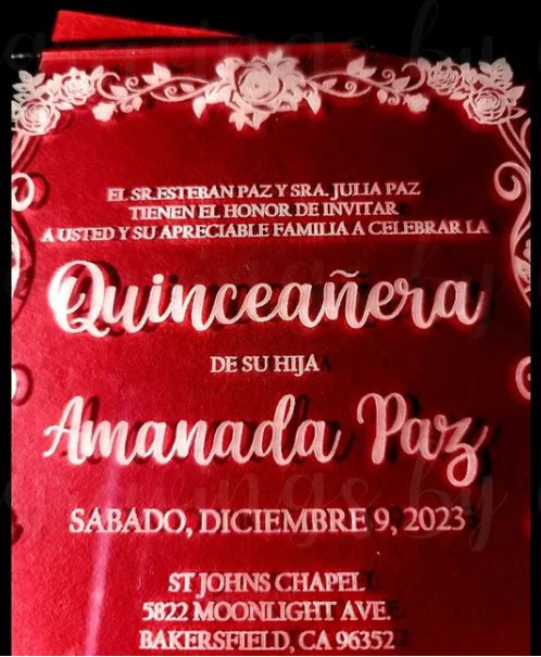 Thumbnail: A clear acrylic quinceañera invitation with elegant white text and floral border detailing is displayed over a vibrant red background. The invitation announces Amanda Paz’s quinceañera celebration with event details in both Spanish and English, creating a bold and festive presentation.
