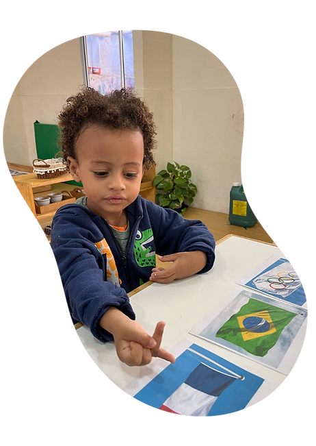 Criança identificando bandeiras de diferentes países em atividade de geografia com cartões educativos em sala de aula Montessori na escola do Tatuapé em São Paulo.