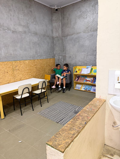 Crianças sentadas em cantinho de leitura com estante de livros em ambiente preparado da sala Montessori na escola do Tatuapé em São Paulo.