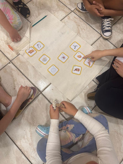 Crianças participando de atividade de vocabulário com cartões ilustrados sobre tapete de trabalho, desenvolvendo linguagem e associação de palavras em ambiente Montessori na escola do Tatuapé em São Paulo.