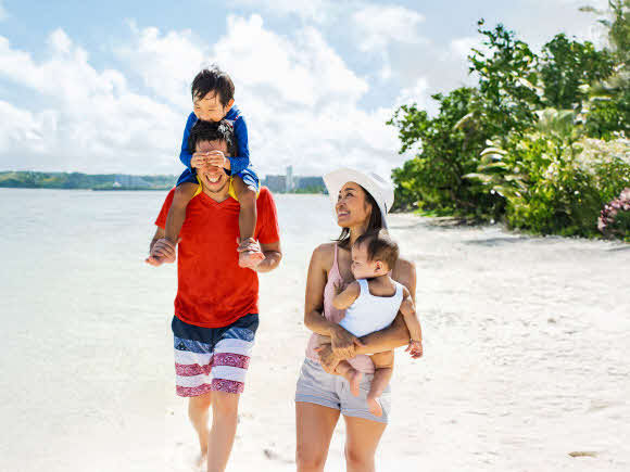 Family walking on beach in Vietnam with baby and toddler being carried by Mum and Dad during family holiday with parents nearby