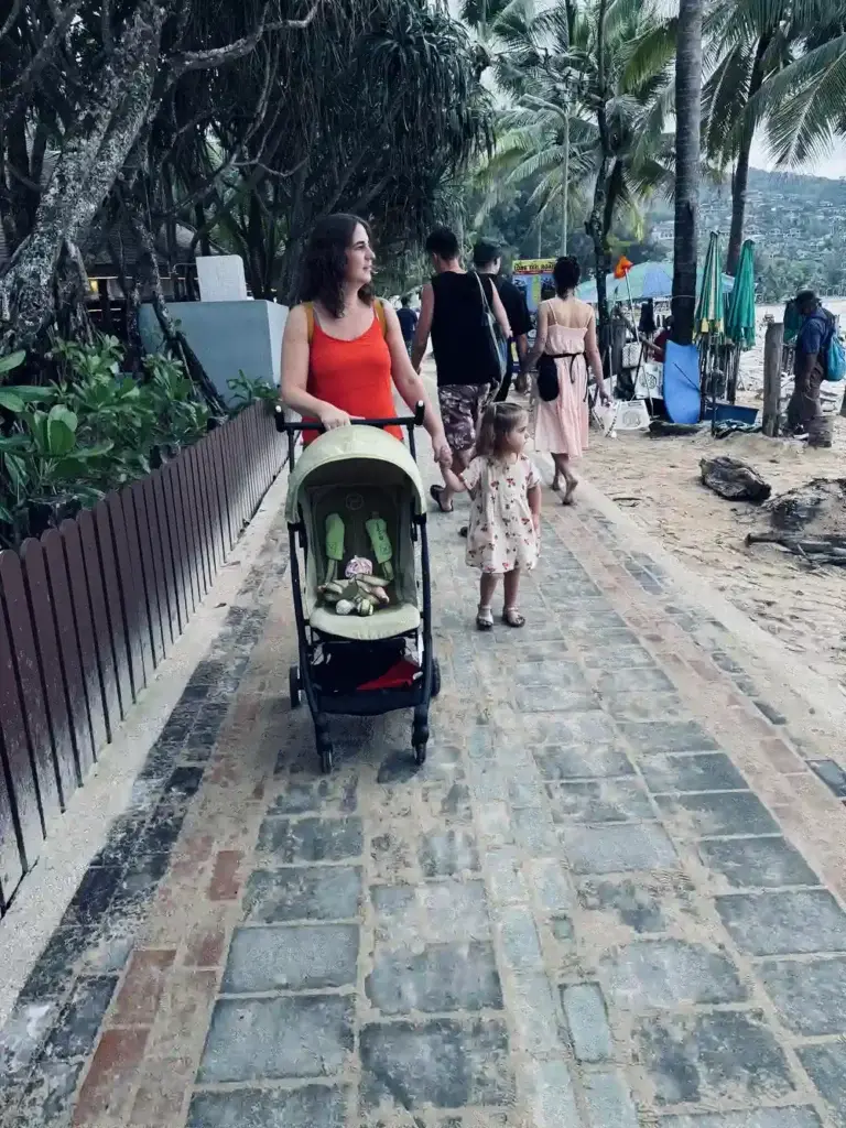 Family pushing stroller along Phuket beachfront walkway Thailand with toddler