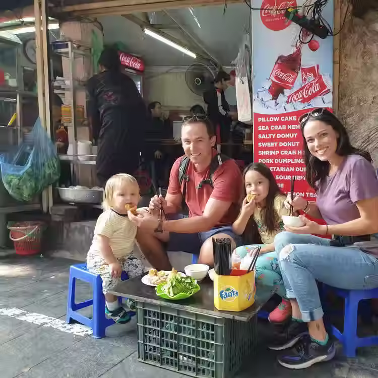 Family eating hot pho at a busy Vietnam street food stall in the morning