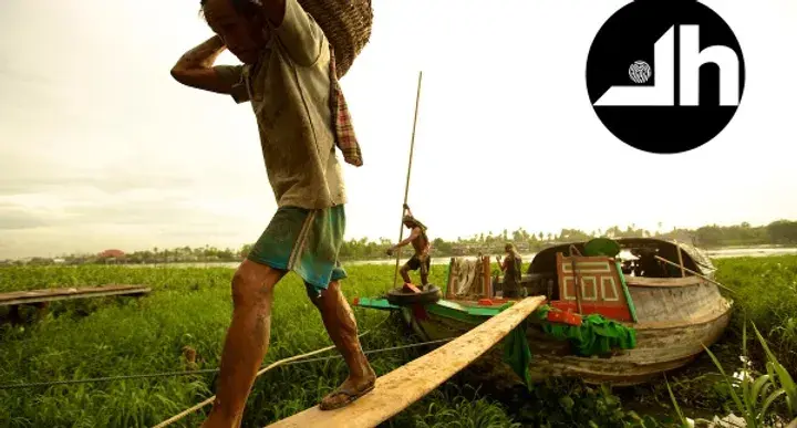 Man carrying goods on a wooden boat in a riverside village, photograph by Casey Templeton.