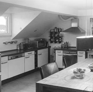 Küche unterm Dach mit Backofen, Schränken und Tisch. Auf einem Tisch eine Obstschale.